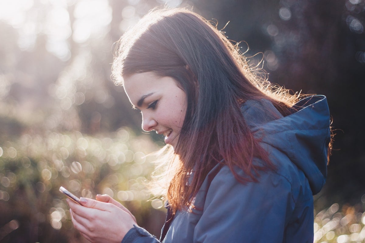 Young woman smiling at her phone outdoors